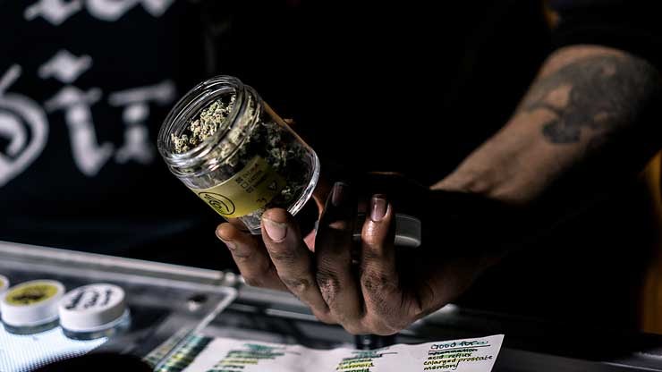 A budtender shows a jar of cannabis alongside a list of recommended uses. (Brandon Crawford)