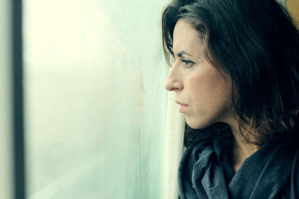 An anxious woman looking out the window of her apartment