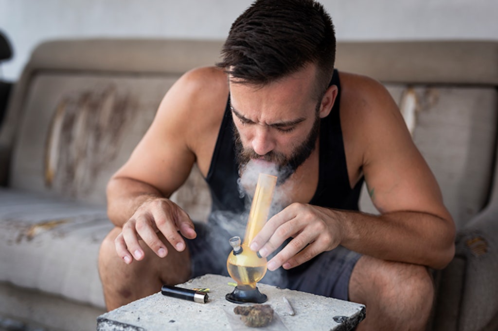 Homem fuma cannabis com bong de vidro.