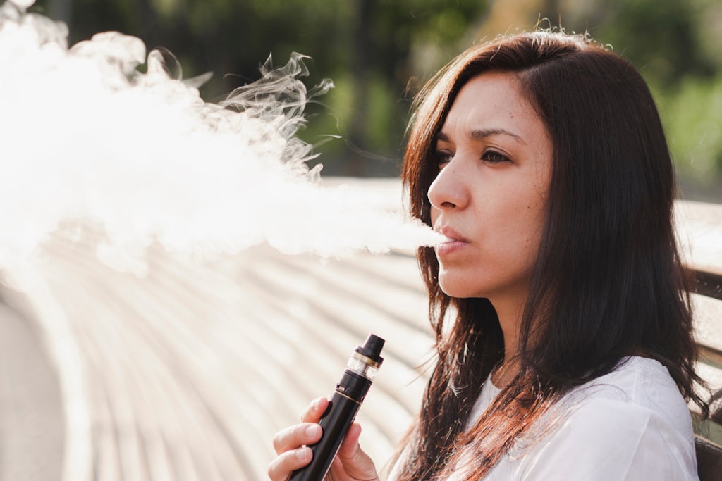 Young woman sitting on a bench and vaping