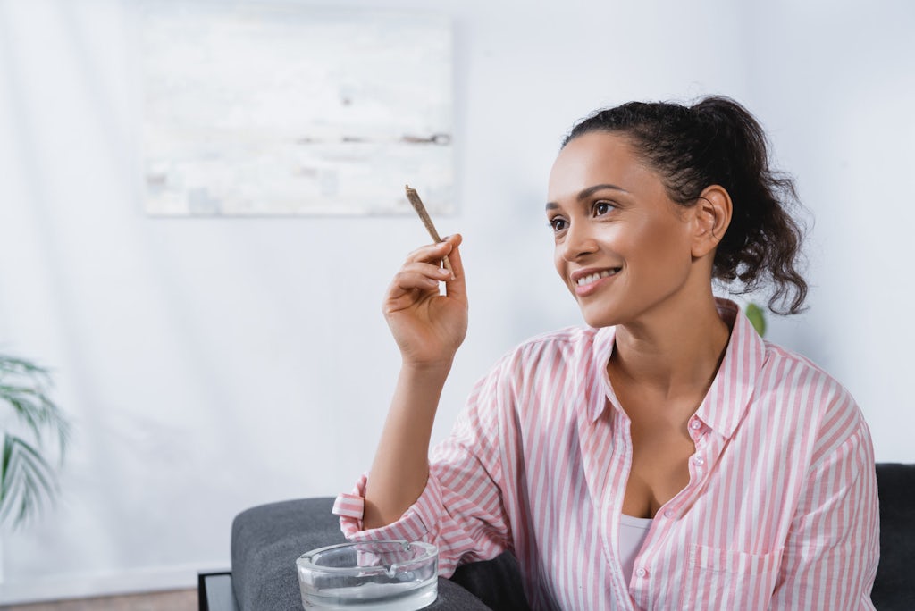 Young woman smiling and holding a joint next to an ashtray