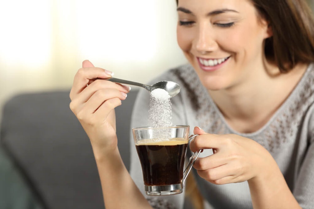 A woman pours a teaspoon of sugar into her coffee