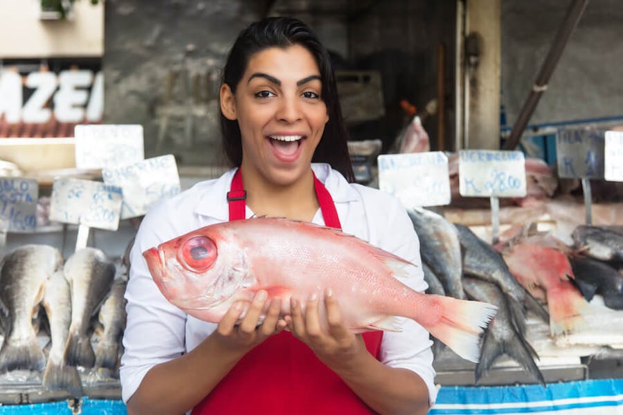 A woman holds up a fish at a fish market