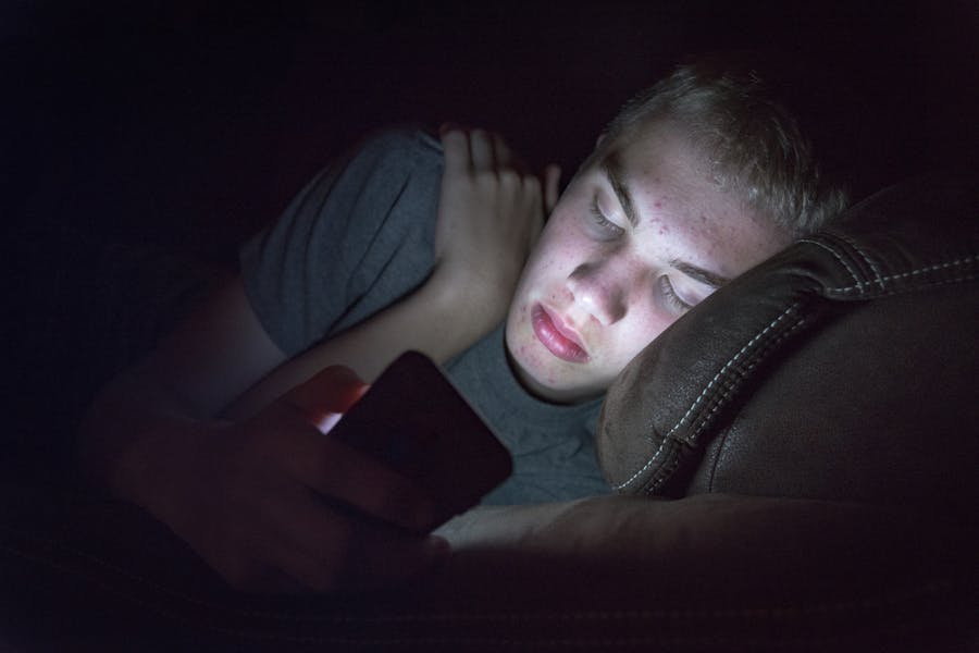 A teenage boy on his phone in bed instead of sleeping